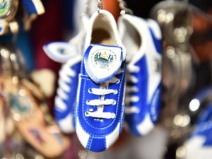 Llavero con forma de zapatilla deportiva azul y blanca con el escudo salvadoreño.